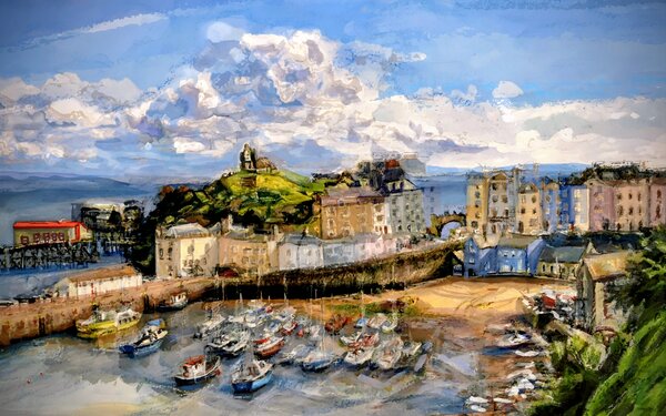 Tenby Harbour at low tide with boats below pastel-coloured buildings under a wide sky.